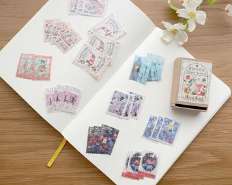 May include: A collection of colorful, illustrated postage stamps featuring whimsical designs, including a fairy, a gnome, a house, and a sleeping beauty. The stamps are arranged on a white notebook with a yellow ribbon.