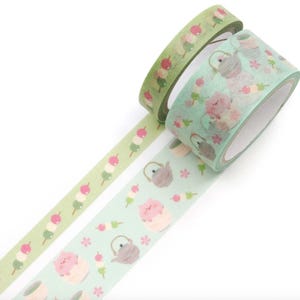 May include: Two rolls of decorative washi tape. One roll is light green with a pattern of dango, a Japanese sweet treat. The other roll is light teal with a pattern of teapots, pigs, and flowers. The tape is ideal for scrapbooking and crafts.