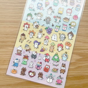 以下が含まれることがあります： 様々な季節の衣装を着た、かわいい漫画の猫が描かれたステッカーシート。ステッカーは3列に配置されており、各列は春、秋、冬の異なる季節を表しています。ステッカーは透明なプラスチックに印刷されており、手帳、日記、その他の持ち物に遊び心を加えるのに最適です。