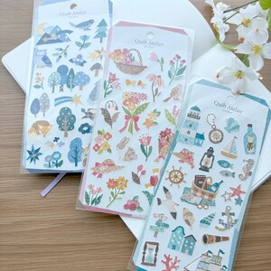 May include: Three clear plastic sheets of Quilt Atelier stickers featuring various designs. The left sheet displays blue-toned nature motifs, the center sheet shows floral and rabbit illustrations, and the right sheet depicts nautical and seaside icons.