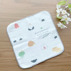 May include: White cotton hand towel with a gray border. The towel has a cute cartoon design of various onigiri (Japanese rice balls) with faces. The text "yuru musubi" is written on the towel, along with the words "obento friends" and "minna yummy".
