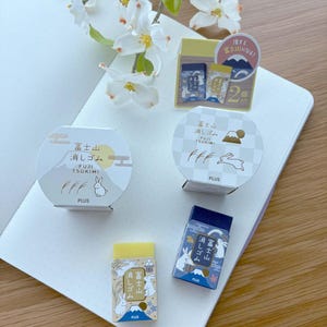 May include: An assortment of Japanese erasers featuring illustrations of Mount Fuji and rabbits. The erasers are in various shapes and sizes, with packaging in white, yellow, and blue. The text on the packaging includes Japanese characters and the word "PLUS".