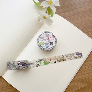 May include: A roll of decorative washi tape with a travel theme. The tape features a variety of illustrations, including airplanes, bicycles, buses, and a compass. The tape is 15mm wide and 3 meters long. The tape is designed by Shinz and is called "Kirapika Travel Masking Tape".