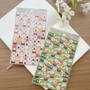 May include: Two sheets of stickers with a Japanese theme. One sheet features 112 pink and white onigiri (rice balls) with various fillings. The other sheet features 98 green and white sushi rolls with various fillings. Both sheets have the text "CIRCLE SEALS" on them.