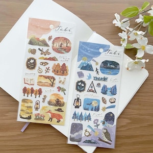 May include: Two sheets of stickers featuring illustrations of nature scenes. The first sheet has a fall theme with a fox, trees, and a lantern. The second sheet has a night sky theme with an owl, mountains, and a starry sky. Both sheets have the text "Tabi" and "And We Are The Explorers".
