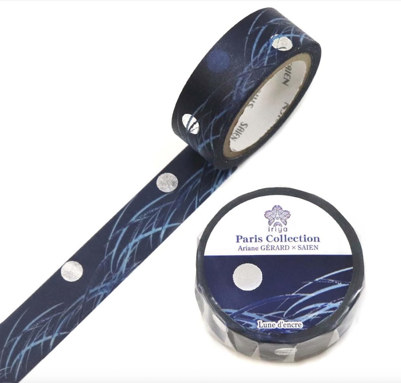 May include: A roll of decorative washi tape with a navy blue background and a pattern of silver circles and light blue lines. The tape is labeled "Paris Collection" with the text "Lune d'encre".