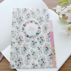 May include: A translucent plastic document folder featuring a repeating pattern of small pink and green wildflowers. The center displays a circular floral wreath enclosing the text Floral composition. The right edge has three colored index tabs.