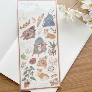 May include: A sheet of stickers featuring illustrations of a dog, a chair, a loaf of bread, a jar of jam, a potted plant, and other homey details. The stickers are on a white background with the text "Snug Room" and "Bread" at the top.