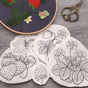 Può includere: Cinque motivi di ricamo per un motivo di fragola. I motivi sono stampati su tessuto bianco e presentano contorni di fragole, foglie e fiori.