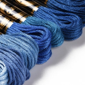 May include: A close-up of several spools of blue embroidery floss, arranged in a gradient from light to dark blue.