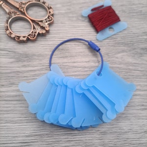Puede incluir: Un juego de 10 bobinas de hilo de plástico azul en un cordón azul. Las bobinas están diseñadas para sujetar hilo para bordar u otras manualidades.