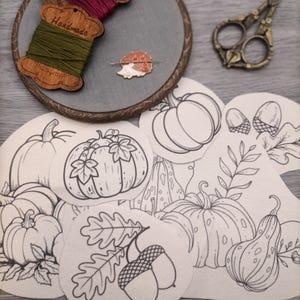 May include: A set of eight embroidery patterns featuring autumnal themes, including pumpkins, acorns, and leaves. The patterns are printed on white fabric and are ready to be stitched.