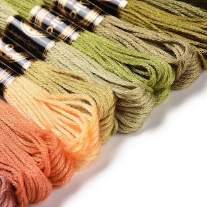 May include: A close-up of a collection of embroidery floss spools in various shades of green, orange, and brown. The spools are arranged in a gradient pattern, with the darkest shades at the bottom and the lightest shades at the top.