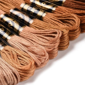 May include: A close-up of a collection of embroidery floss spools in various shades of brown. The spools are labelled "DMC" and "Embroider" with a gold background and black lettering.