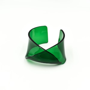 Könnte beinhalten: Ein grünes, verdrehtes Plastik-Armband. Das Armband besteht aus einem einzigen Stück Plastik, das zu einer einzigartigen Form gebogen und verdreht wurde.