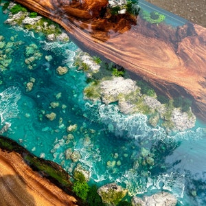 K&ouml;nnte beinhalten: Nahaufnahme eines Holztisches mit einem t&uuml;rkisblauen Epoxid-Fluss, der durch die Mitte verl&auml;uft. Der Epoxid-Fluss ist mit wei&szlig;en Wirbeln und kleinen, runden, grauen Steinen gef&uuml;llt. Das Holz ist in einem satten Braun mit einer nat&uuml;rlichen Maserung.