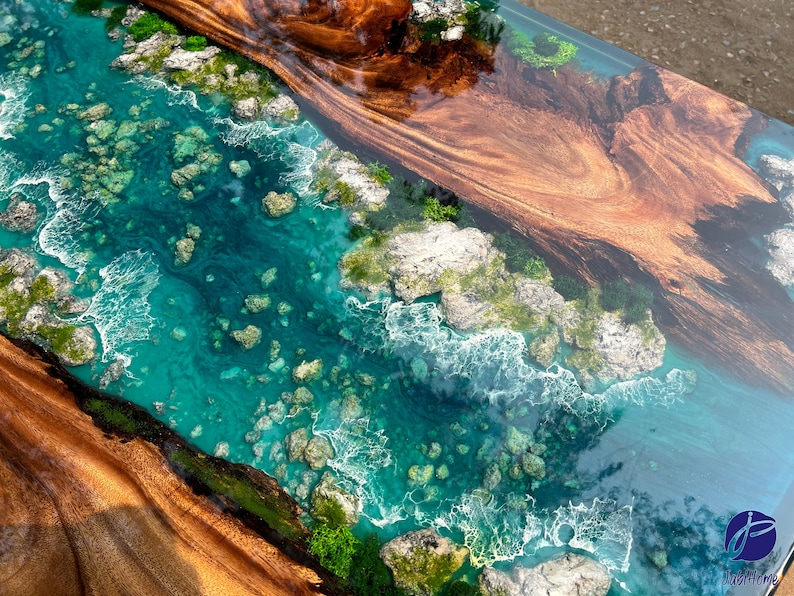 K&ouml;nnte beinhalten: Nahaufnahme eines Holztisches mit einem t&uuml;rkisblauen Epoxid-Fluss, der durch die Mitte verl&auml;uft. Der Epoxid-Fluss ist mit wei&szlig;en Wirbeln und kleinen, runden, grauen Steinen gef&uuml;llt. Das Holz ist in einem satten Braun mit einer nat&uuml;rlichen Maserung.