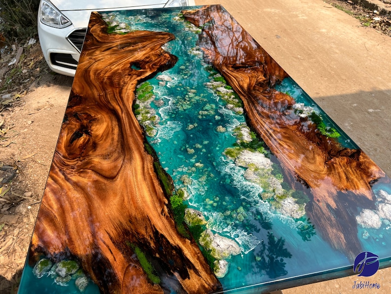 K&ouml;nnte beinhalten: Eine Tischplatte aus Holz mit einem Fluss aus blauem Epoxidharz, der durch sie flie&szlig;t. Das Harz hat wei&szlig;e und gr&uuml;ne Akzente, die an Wellen und Algen erinnern.