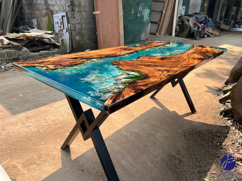 K&ouml;nnte beinhalten: Ein Holztisch mit einem blauen und gr&uuml;nen Epoxidharzeinlege. Der Tisch hat ein schwarzes Metallgestell mit einem kreuzf&ouml;rmigen Design.