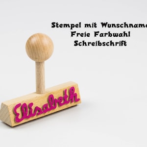 Könnte beinhalten: Ein Stempel aus Holz mit einem rosa Gummieindruck des Namens "Elisabeth". Der Stempel hat einen Holzgriff und befindet sich auf weißem Hintergrund. Der Text "Stempel mit Wunschname Freie Farbwahl Schreibschrift" ist oberhalb des Stempels sichtbar.