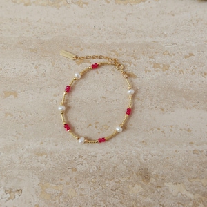 May include: A gold bracelet with a delicate chain and alternating red and white beads.