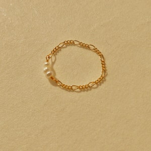 May include: A delicate gold chain ring featuring three small white pearls. The ring is crafted from a simple, yet elegant, chain design.