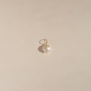 Op de afbeelding: Een witte parel hanger met een gouden lus om aan een ketting of armband te bevestigen.