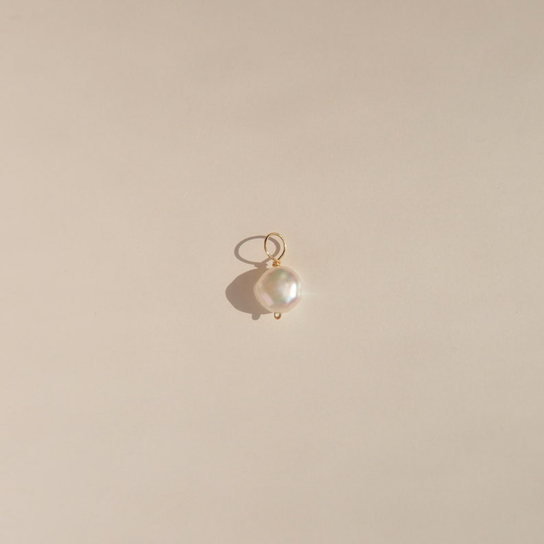 May include: A white pearl pendant charm with a gold loop for attaching to a necklace or bracelet.