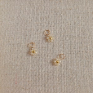Op de afbeelding: Drie goudkleurige bedels met witte parel-madeliefjes. De bedels hebben een kleine lus aan de bovenkant om aan sieraden te bevestigen.