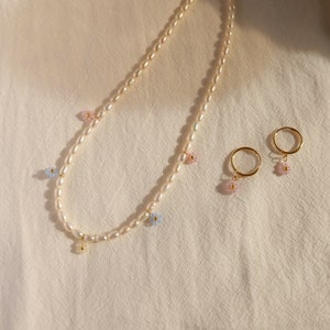 Op de afbeelding: Een parelketting met kleine bloembedels in roze, blauw en wit. Twee bijpassende bloembedels oorbellen zijn ook inbegrepen.