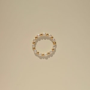 Puede incluir: Un brazalete de cuentas doradas y blancas con un diseño circular.