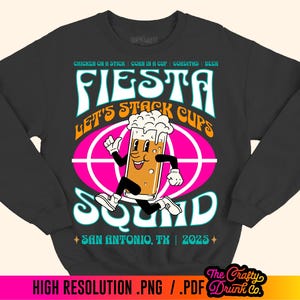 May include: Black sweatshirt with a pink, blue, and yellow graphic design. The graphic features a cartoon beer mug with a face and the text "Fiesta Let's Stack Cups Squad" and "San Antonio, TX | 2023".