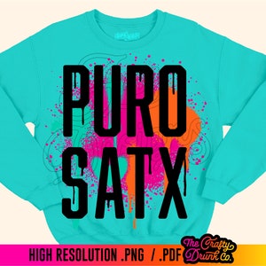 May include: A turquoise blue sweatshirt with a black graphic print that says "PURO SATX" in a dripping paint style. The graphic is surrounded by pink, orange, and white paint splatters.