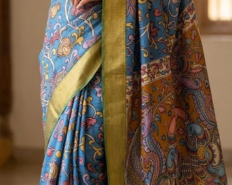 May include: A blue saree with a floral and paisley pattern, accented with gold trim. The fabric features a detailed design with shades of blue, yellow, pink, and orange. The saree's border is a contrasting gold.