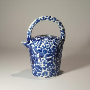 May include: A ceramic teapot with a white and blue spotted pattern. The teapot has a curved handle and a spout. The lid also has the same blue and white spotted pattern. The teapot is a light blue and white color.