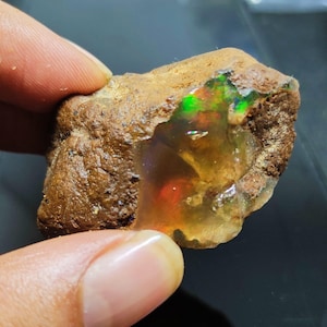 Pode incluir: Uma rocha marrom áspera com um grande opala claro dentro. O opala tem flashes de verde, vermelho e laranja.