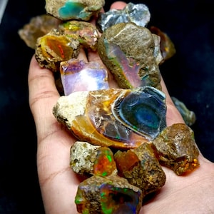 Può includere: Una collezione di pietre di opale grezze in vari colori, tra cui verde, blu, arancione e viola. Le pietre sono incastonate in una matrice di roccia marrone.