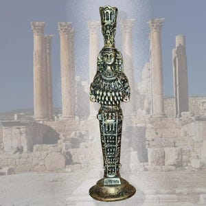 Puede incluir: Una estatua detallada de estilo antiguo de una mujer, posiblemente egipcia, con un tocado alto y ornamentado. La estatua es principalmente verde oscuro y dorada, con detalles intrincados. La base es redonda y dorada. El fondo presenta ruinas antiguas.