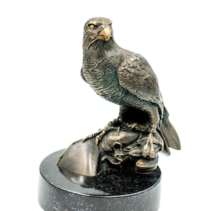 May include: Bronze eagle sculpture perched on a rock, mounted on a black marble base. The eagle has detailed feathering and a focused gaze. A decorative item for home or office.