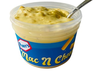 Puede incluir: Un recipiente de plástico transparente lleno de salsa de macarrones con queso amarilla. El recipiente tiene una etiqueta azul con el texto "Pmky's Mac N Cheese".
