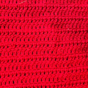 May include: Close-up of a vibrant red crocheted fabric. The texture reveals a series of horizontal rows with evenly spaced, open stitches. The bright color and detailed stitching suggest a handmade item, possibly a scarf or blanket.