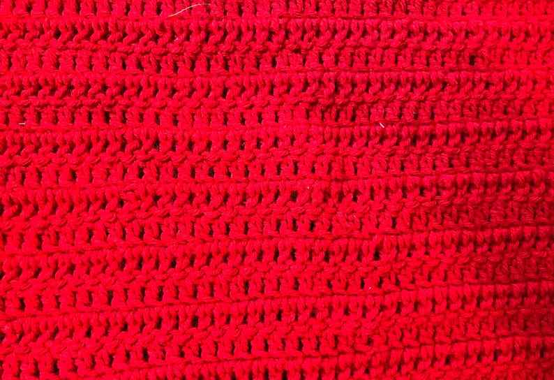 May include: Close-up of a vibrant red crocheted fabric. The texture reveals a series of horizontal rows with evenly spaced, open stitches. The bright color and detailed stitching suggest a handmade item, possibly a scarf or blanket.