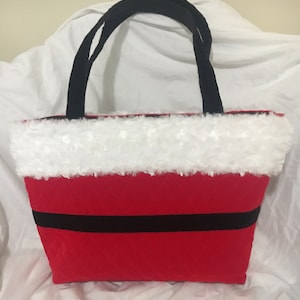 May include: Red tote bag with black handles and a black stripe. The top edge is trimmed with white faux fur. The bag is designed to resemble Santa Claus's suit.