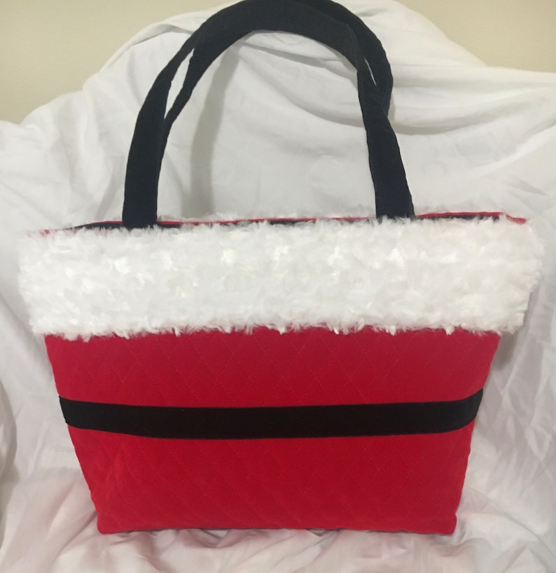 May include: Red tote bag with black handles and a black stripe. The top edge is trimmed with white faux fur. The bag is designed to resemble Santa Claus's suit.