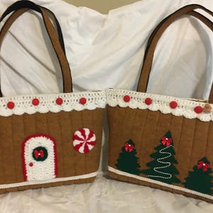 May include: Two brown tote bags with gingerbread house designs. Each bag features a white crocheted trim, red accents, and a black handle. One bag has a door and candy accents, the other has Christmas tree designs.