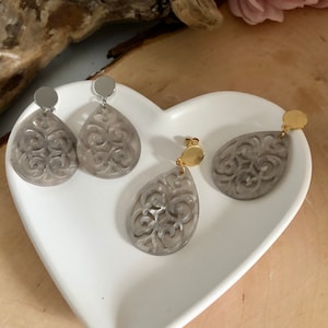 Puede incluir: Un par de pendientes de filigrana grises con postes de plata y oro. Los pendientes tienen forma de lágrima y un diseño delicado e intrincado.