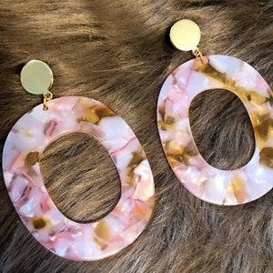 Könnte beinhalten: Ein Paar große ovale Ohrringe mit einem rosa-goldenen Marmormuster. Die Ohrringe haben einen goldfarbenen Metallstecker.