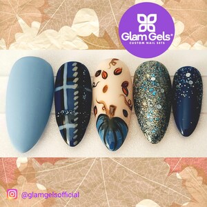 May include: Set of five autumn-themed press-on nails. The nails are a light blue color with different designs, including plaid, a pumpkin, glitter, and a blue and white design. The nails are on a white background with a purple logo that says "Glam Gels" and "Custom Nail Sets".