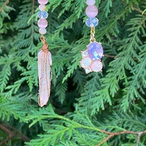 May include: Two pink and clear beaded chains with charms. One charm is a clear crystal point wrapped in copper wire. The other charm is a cluster of pink and clear rhinestones with a purple gemstone in the center.