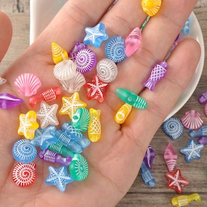 May include: A handful of colorful, translucent beads in various shapes, including starfish, seashells, and fish. The beads are in shades of red, yellow, blue, green, and purple. The beads are small and appear to be made of plastic.